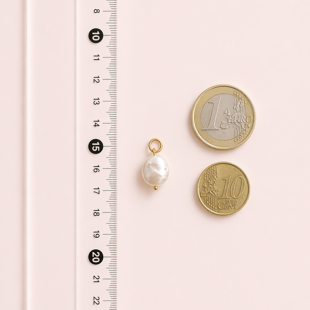 Baroque pearl pendant with two coins on a pink background with a ruler for scale.