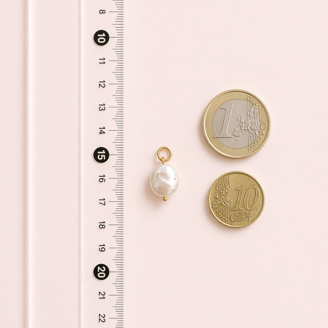 Baroque pearl pendant with two coins on a pink background with a ruler for scale.
