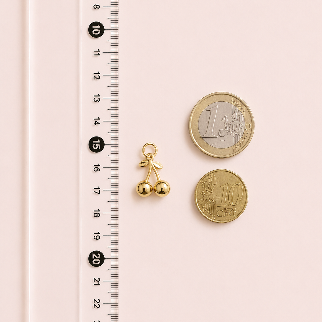 Gold bell charm next to two gold coins on a pink surface with a ruler for scale.