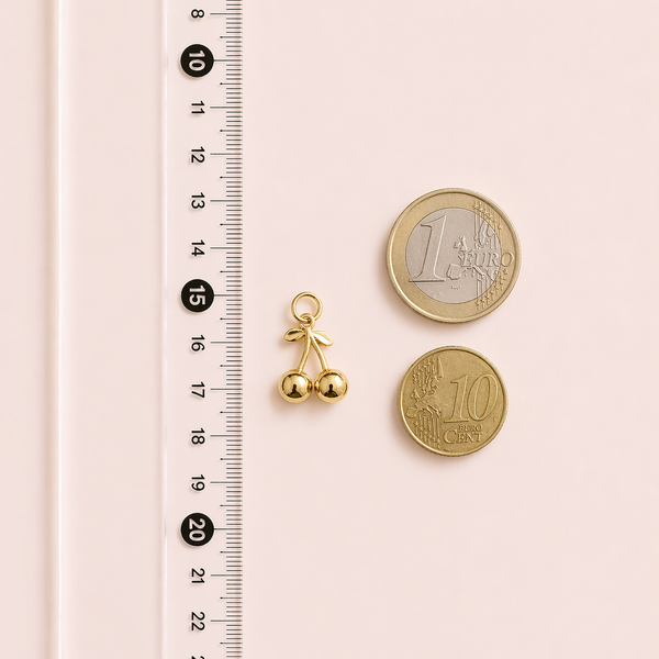 Gold bell charm next to two gold coins on a pink surface with a ruler for scale.