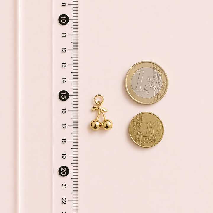 Gold bell charm next to two gold coins on a pink surface with a ruler for scale.