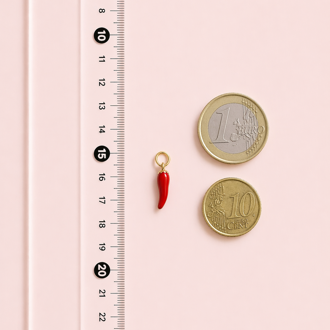Red chili pepper charm next to a €1 coin and a €10 coin on a pink background with a ruler for scale.