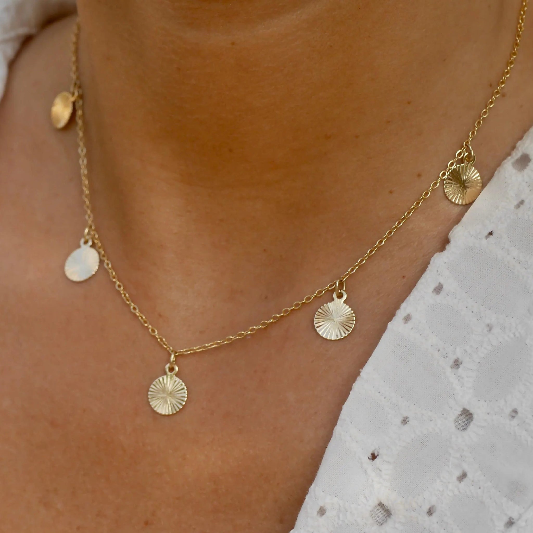 Gold necklace with circular pendants on a person wearing a white lace top.