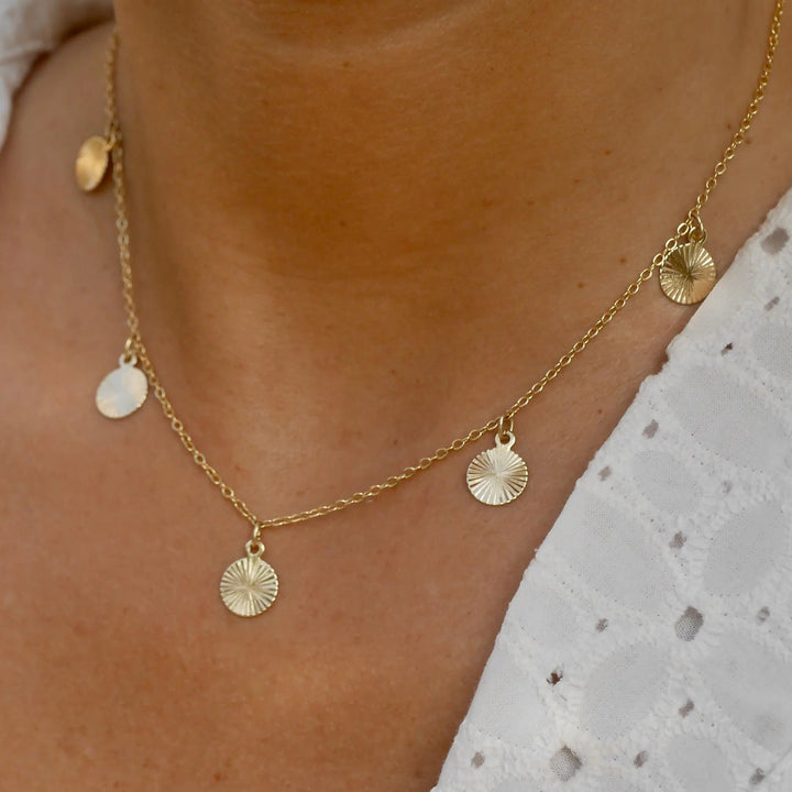 Gold necklace with circular pendants on a person wearing a white lace top.