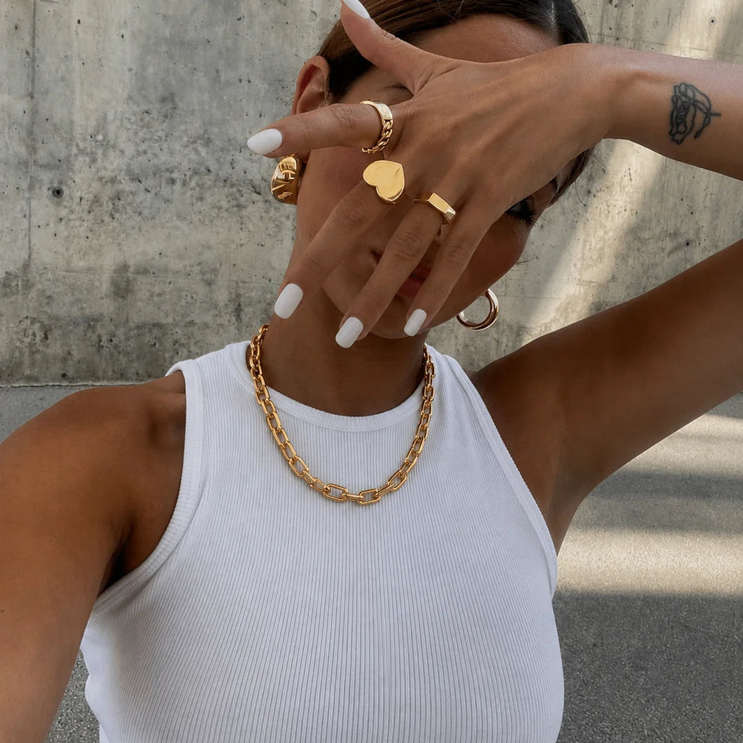 Person wearing gold jewelry with a concrete wall background