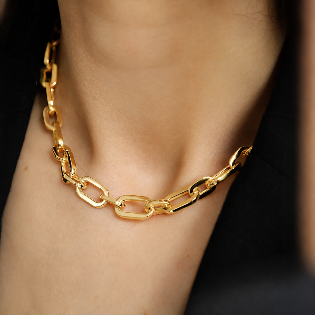 A close-up of a gold chain necklace with large paperclip-style links worn on a person's neck.