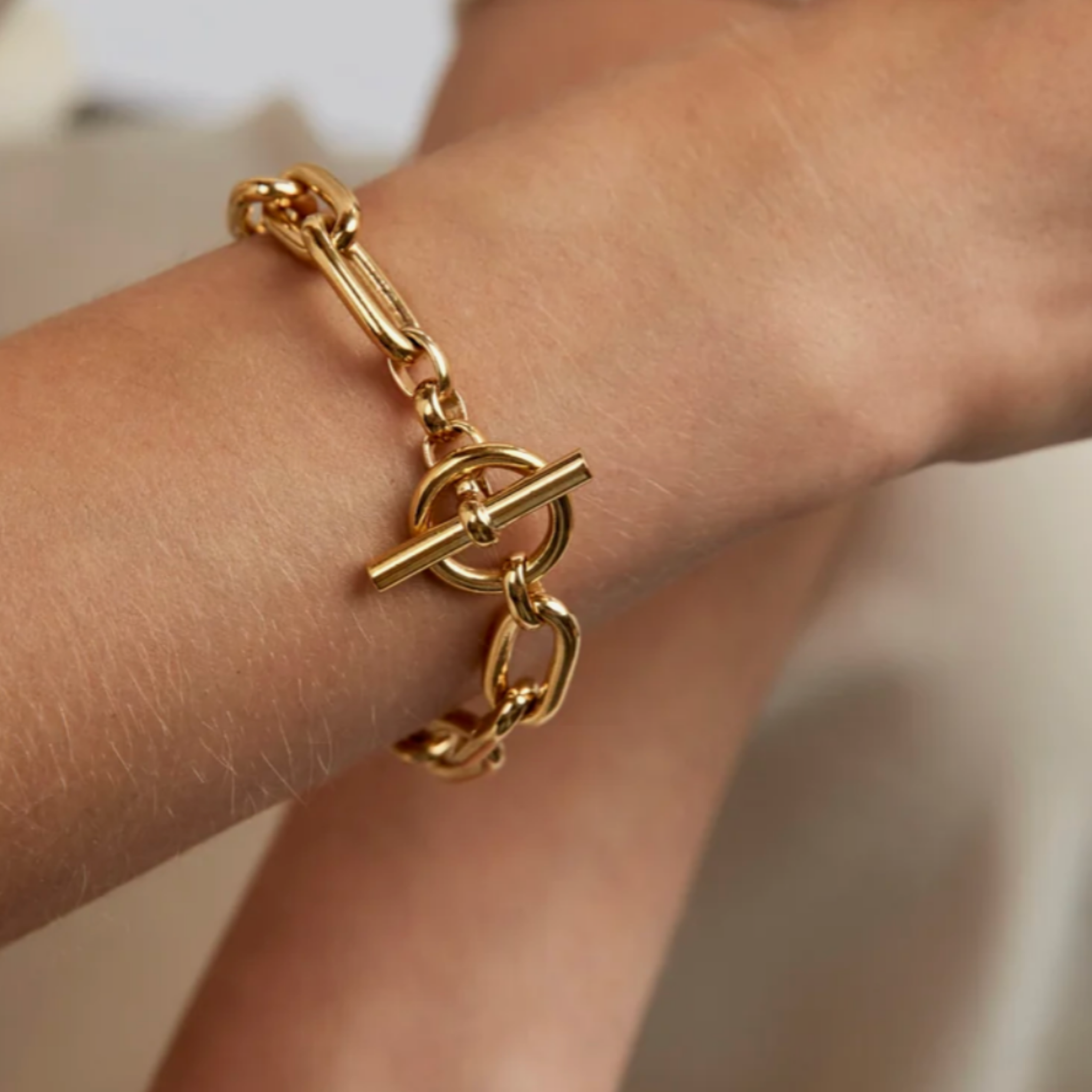 A close-up of a gold chain bracelet with a toggle clasp worn on a person's wrist.