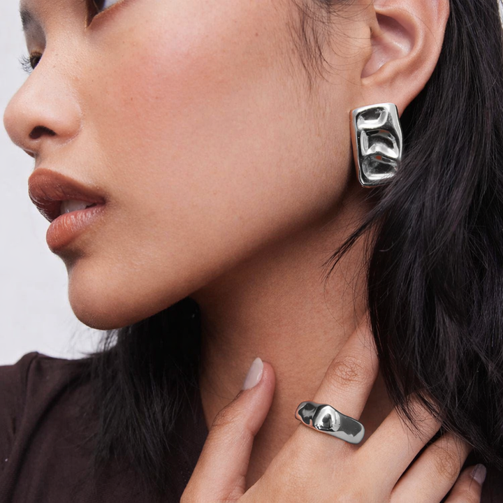Close-up of a woman wearing silver earrings and a ring with a neutral background