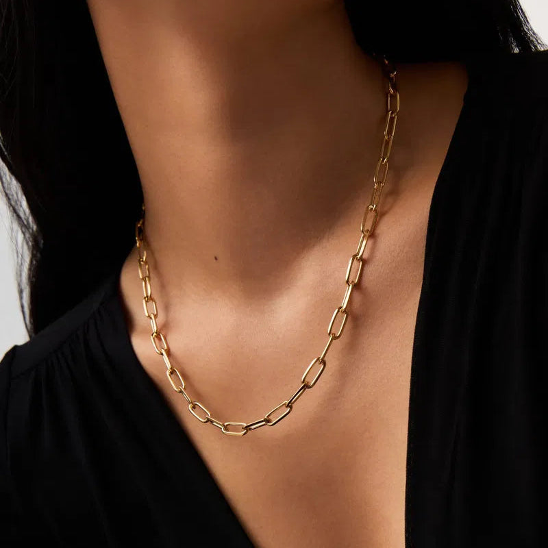 Gold chain necklace worn by a person against a neutral background