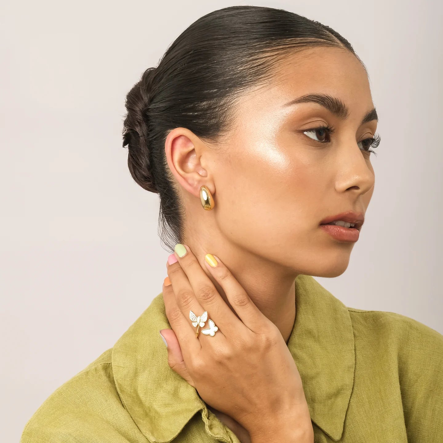 Woman wearing gold earrings and a butterfly ring, with a neutral background