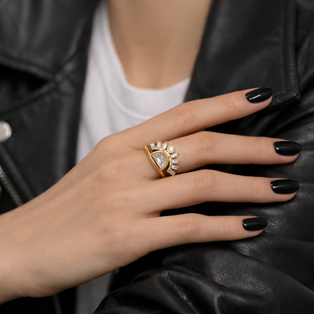 Hand wearing a gold ring with a large gemstone, against a black leather jacket background.