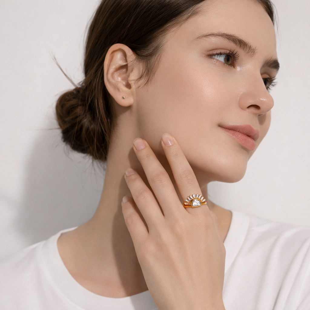 Woman wearing a gold ring with a clear gemstone on a plain background