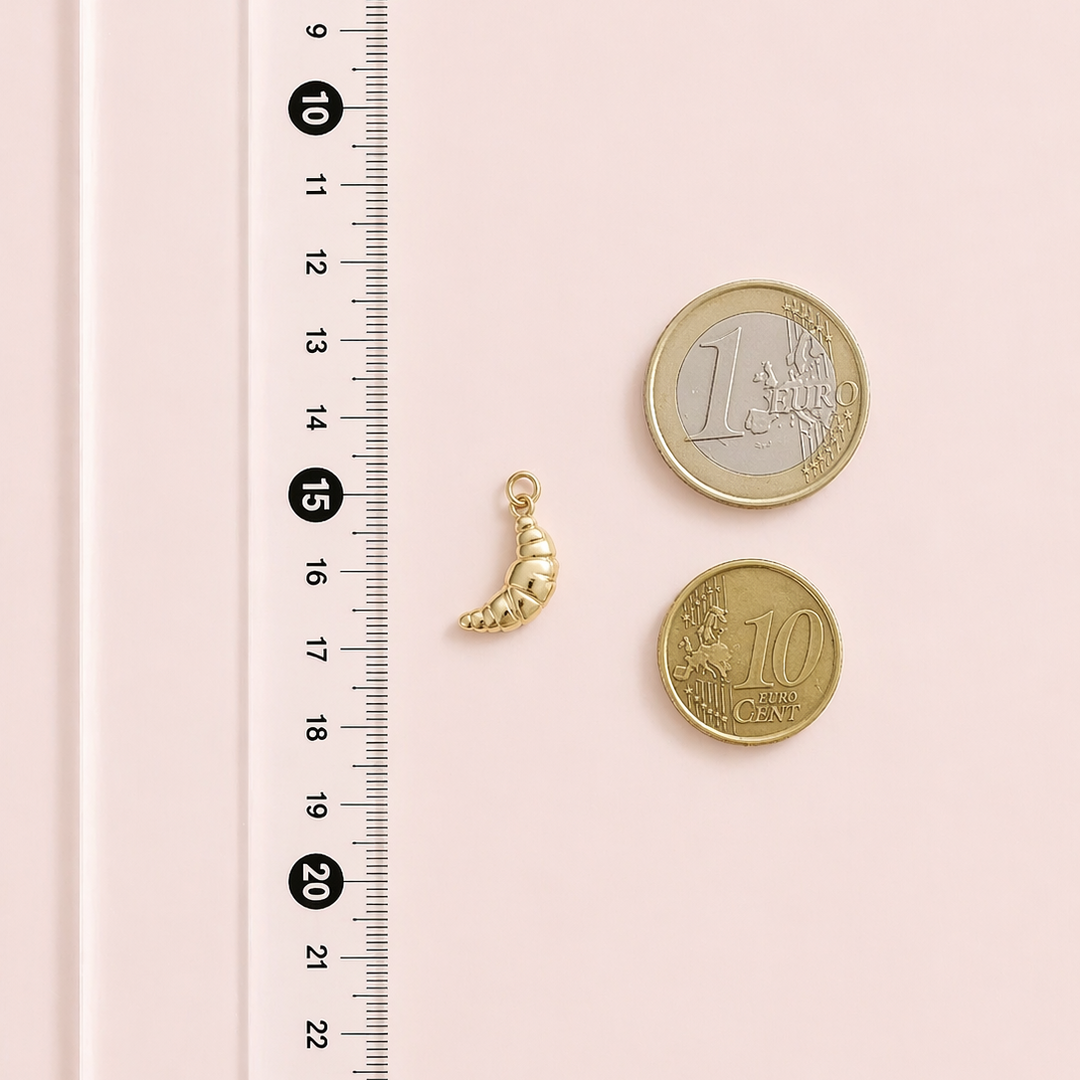 Gold charm and coins on a pink surface with a ruler for scale.