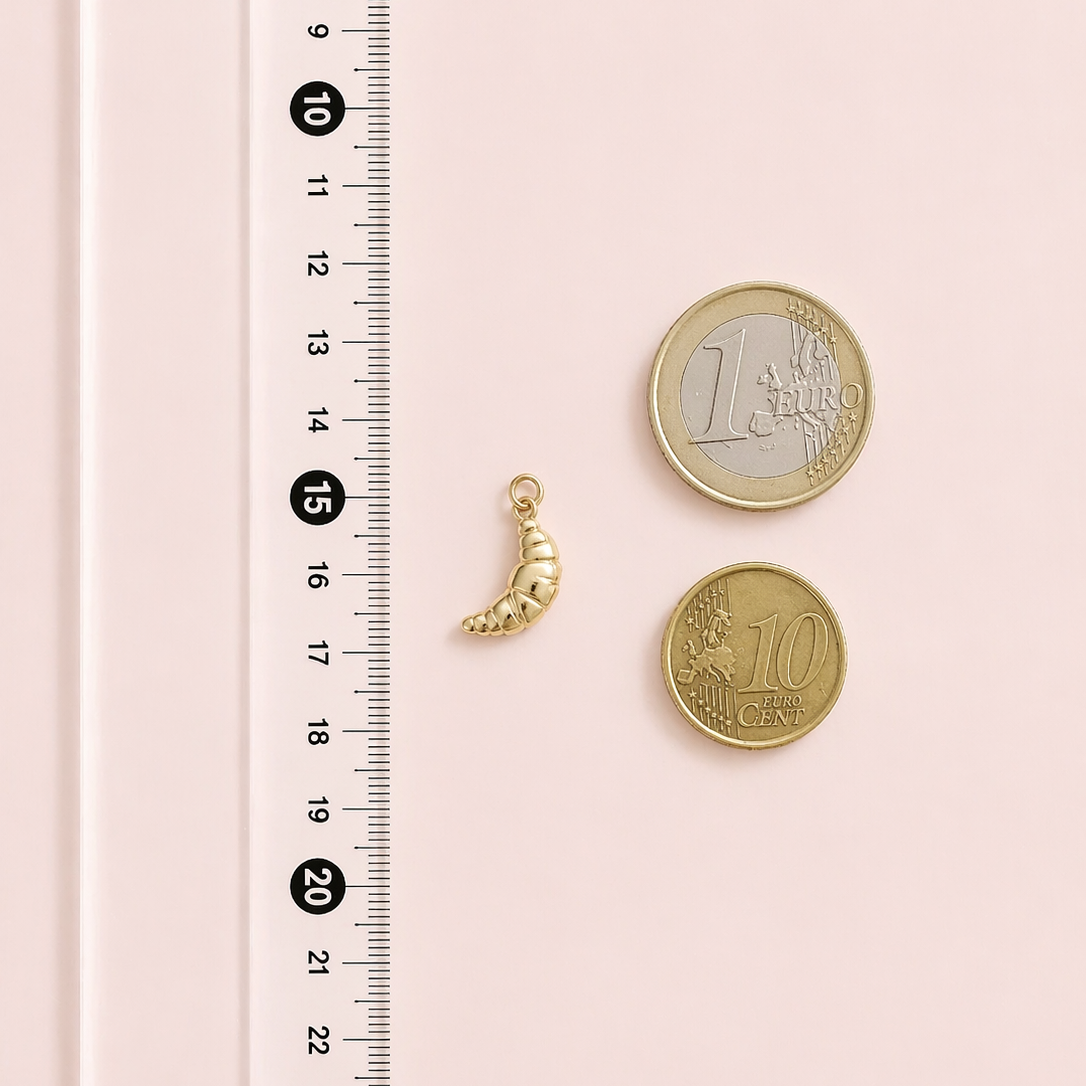 Gold charm and coins on a pink surface with a ruler for scale.