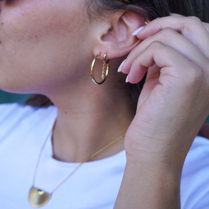 Close-up of a person wearing gold hoop earrings and a necklace, with sunglasses on.