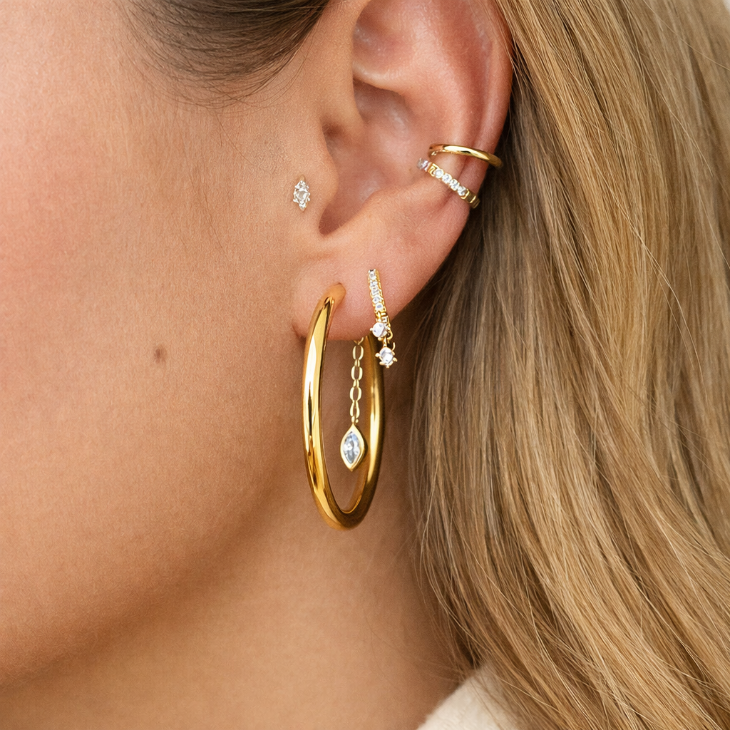 Close-up of an ear wearing gold hoop earrings with small diamond-like stones.