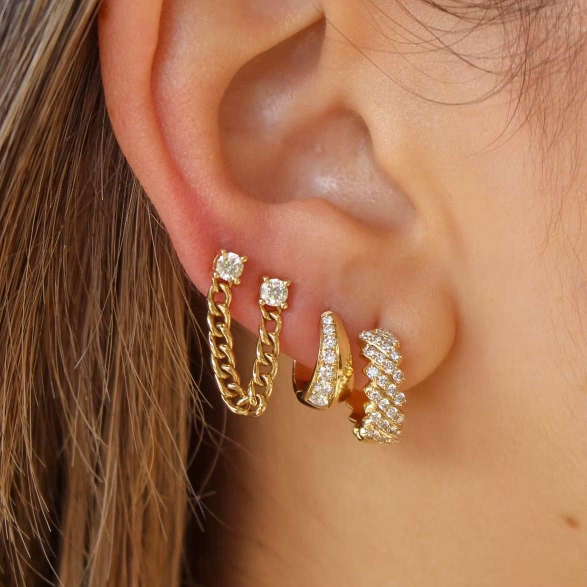 Close-up of an ear wearing gold hoop earrings with clear gemstones.