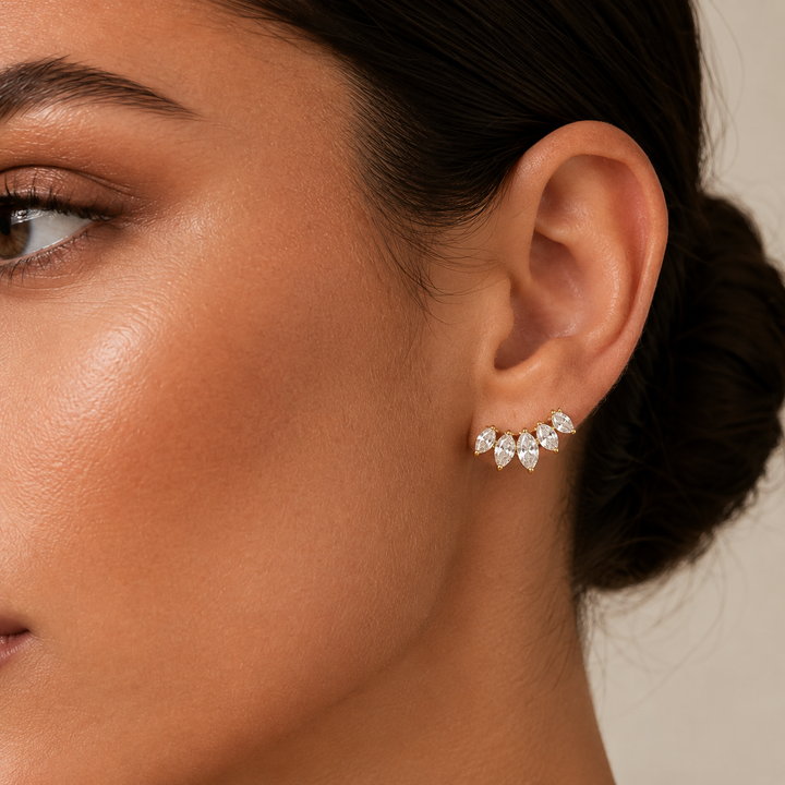 A close-up of a model's ear wearing a small cluster stud earring with marquise-cut clear stones in a silver-toned setting.
