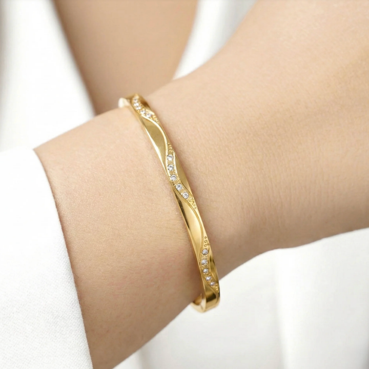 Gold bracelet with small stones on a wrist against a white background