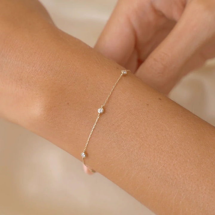 Gold bracelet with small diamonds on a wrist against a neutral background