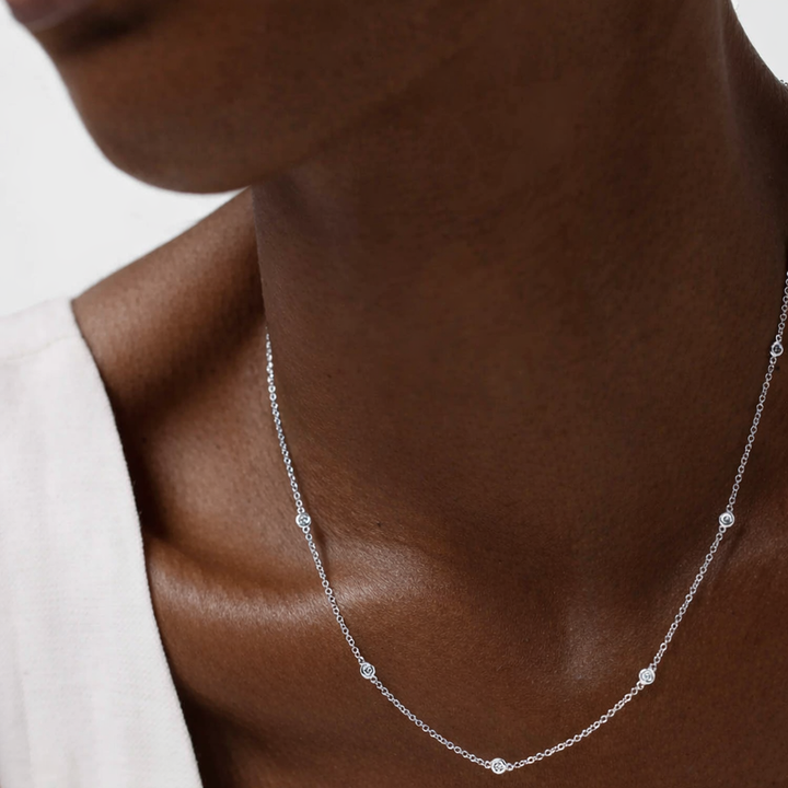 Silver necklace with small diamonds on a person's neck against a neutral background