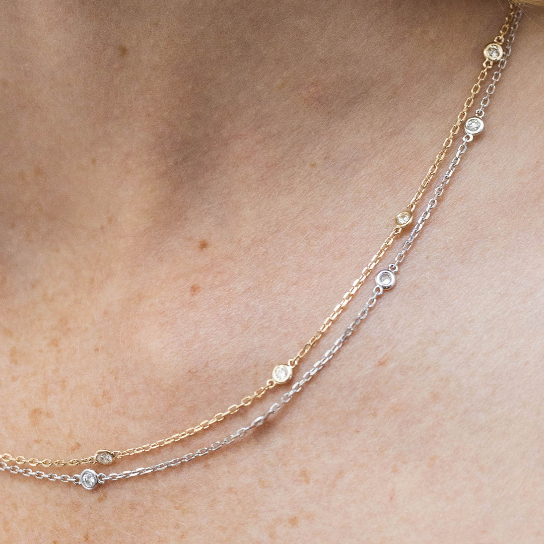 Two delicate necklaces with small beads on a person's neck
