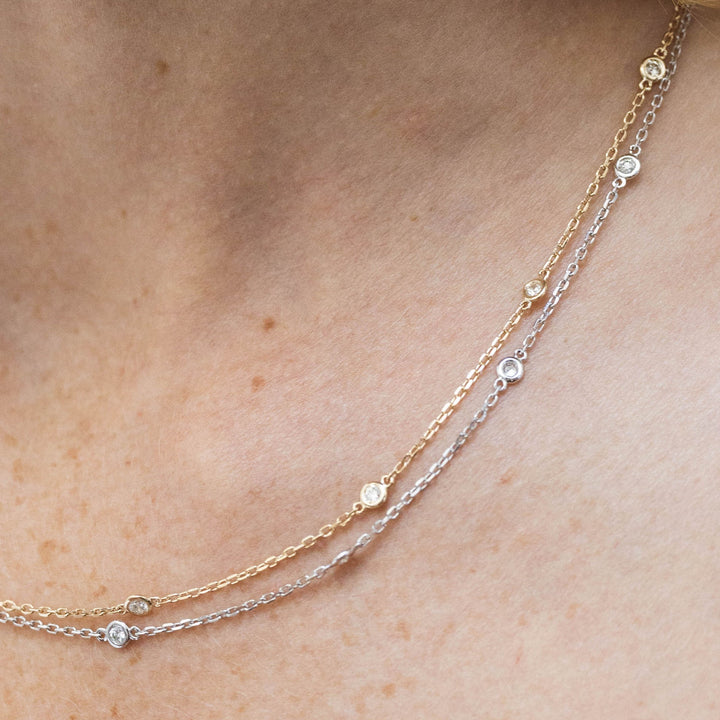 Two delicate necklaces with small beads on a person's neck