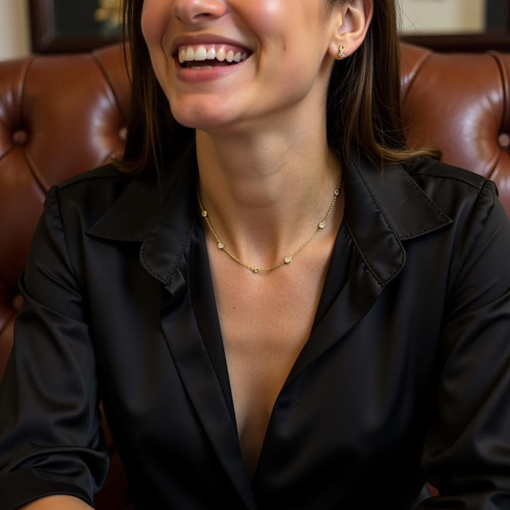 Woman wearing a black blouse with a gold necklace, sitting on a brown leather couch.