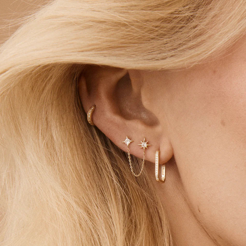 Close-up of an ear with gold earrings against a neutral background