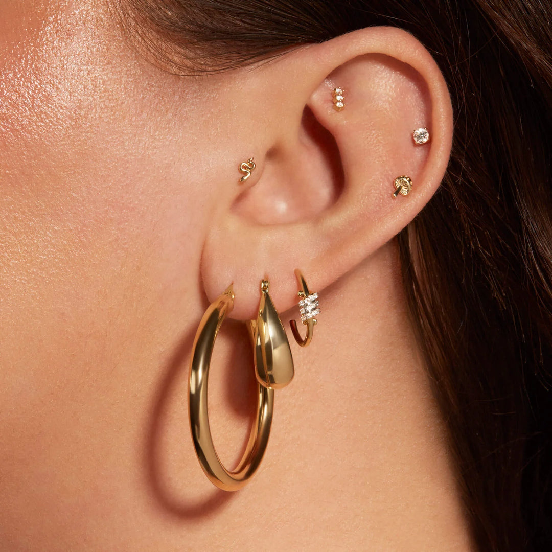 Close-up of an ear with gold hoop earrings and other accessories.
