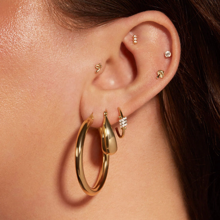 Close-up of an ear with gold hoop earrings and other accessories.