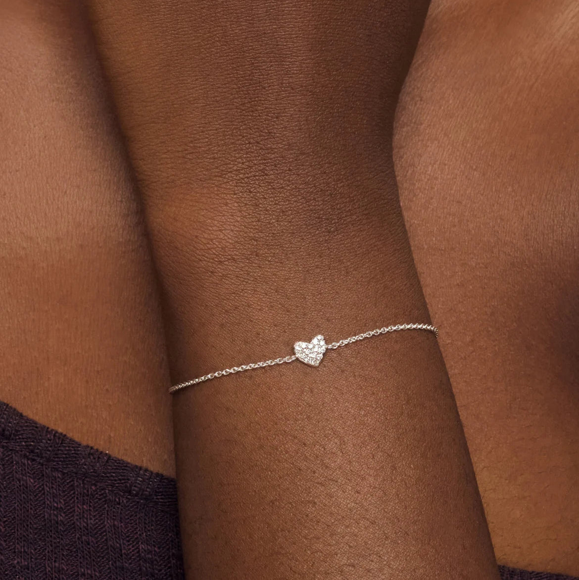 Silver bracelet with a heart-shaped charm on a person's wrist against a brown background