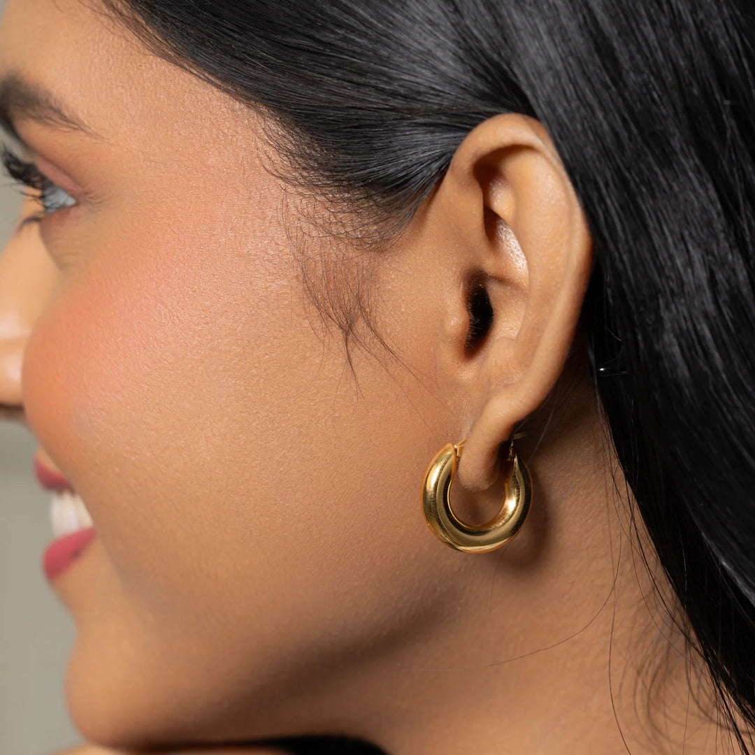 Close-up of a person wearing a gold hoop earring with a neutral background