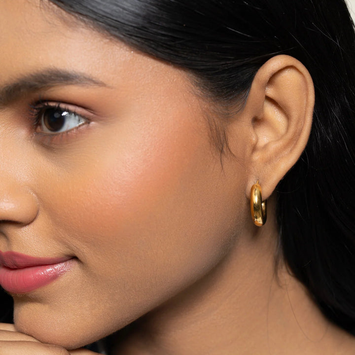 Close-up of a woman wearing gold hoop earrings with a neutral background