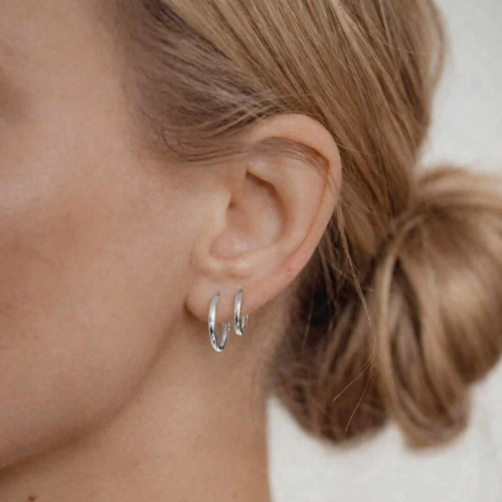 Close-up of a person wearing silver hoop earrings with a neutral background