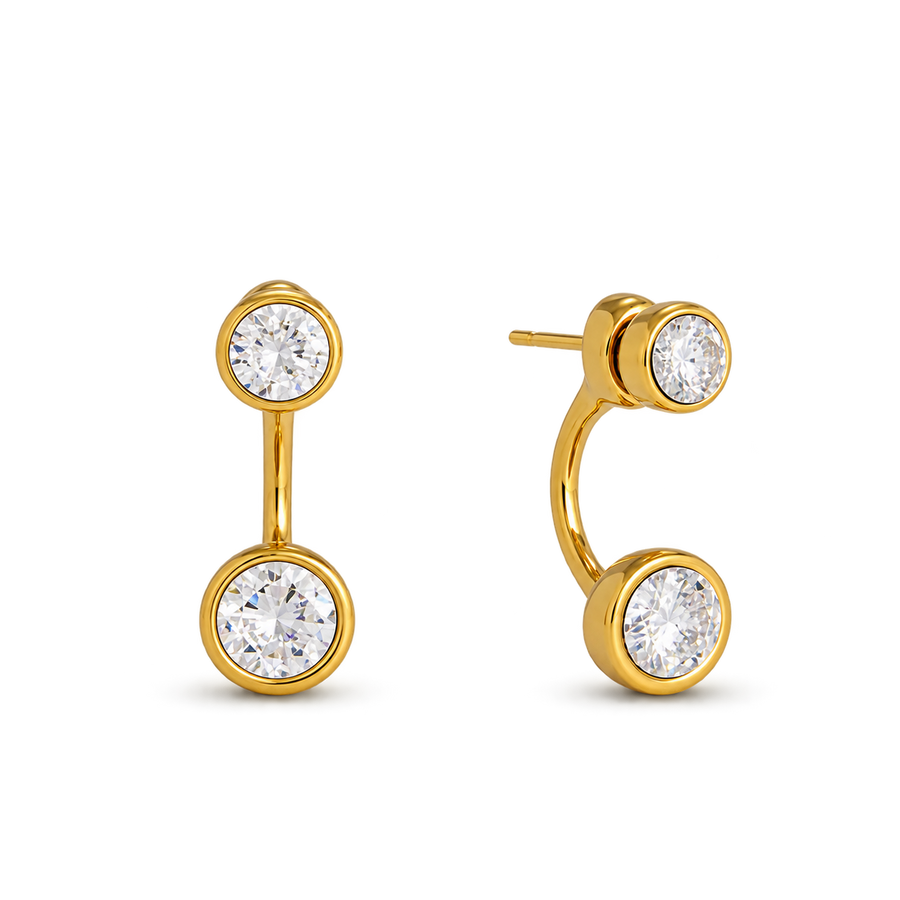 A pair of gold hoop earrings with round bezel-set clear gemstones, shown on a plain white background. One earring is oriented vertically, and the other is angled to show the post and backing.