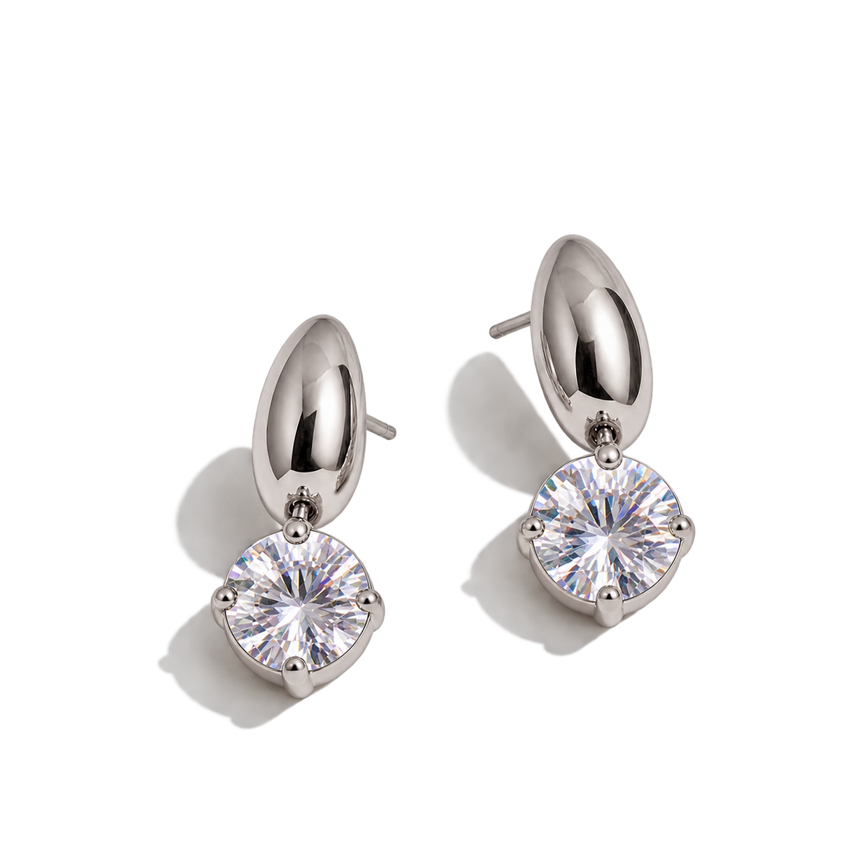 A pair of silver-toned drop earrings with a polished dome-shaped top and a round prong-set clear gemstone below, shown on a clean white background with soft shadows.