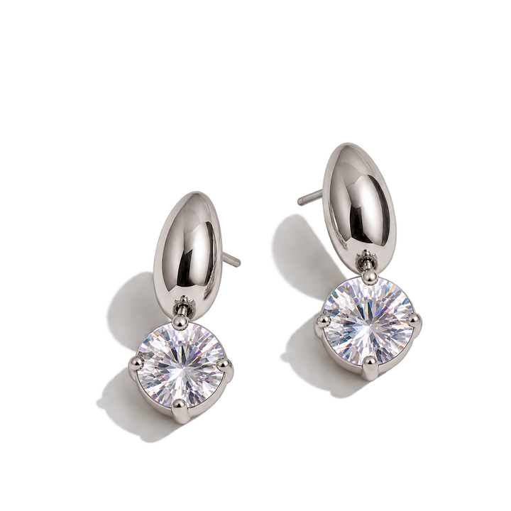 A pair of silver-toned drop earrings with a polished dome-shaped top and a round prong-set clear gemstone below, shown on a clean white background with soft shadows.