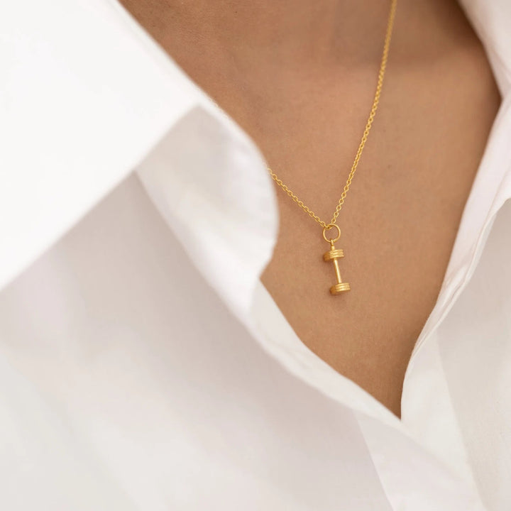 Gold necklace with a small pendant worn by a person in a white shirt.