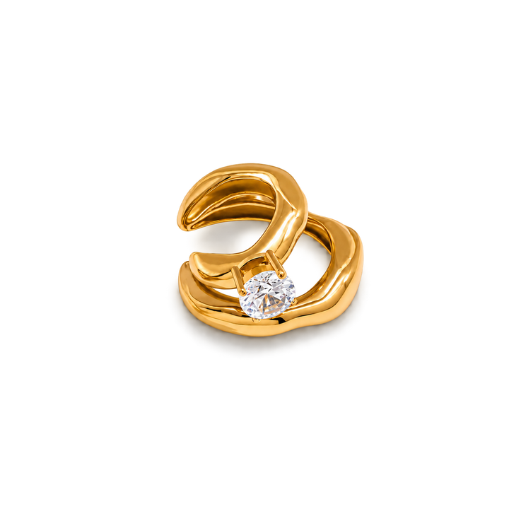 A gold ring with an organic, flowing wavy design and a single round clear gemstone, shown on a plain white background.