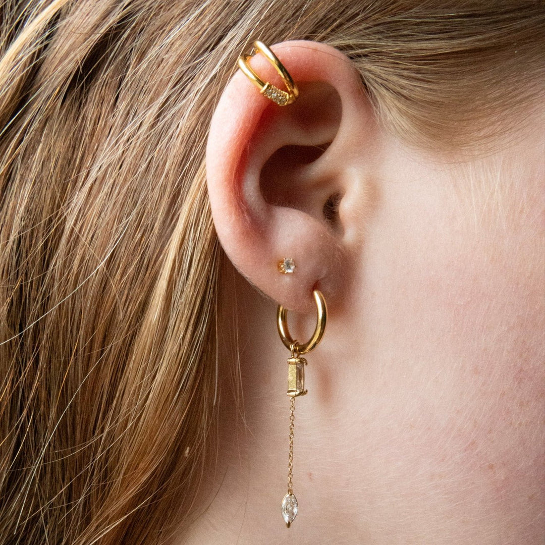 Close-up of a person's ear wearing gold hoop earrings with dangling crystals.
