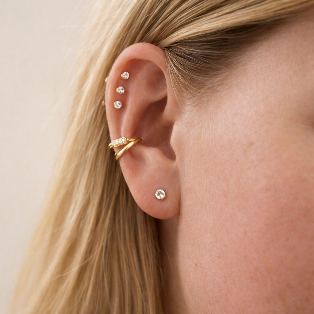 Close-up of an ear with gold and diamond earrings on a neutral background