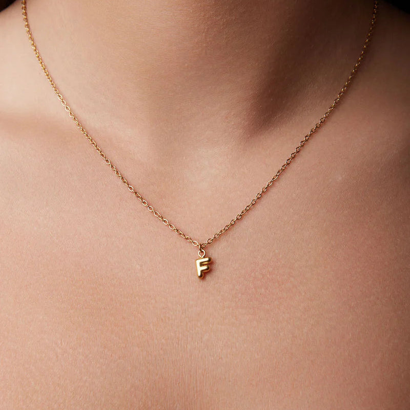 Gold necklace with a 'F' pendant on a person's neck