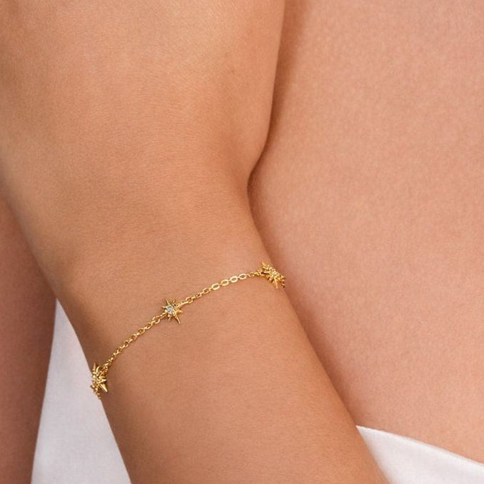 Gold bracelet with star designs on a person's wrist against a neutral background