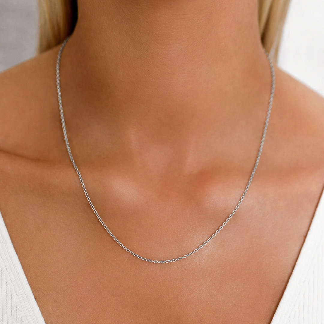Silver necklace on a person wearing a white top against a neutral background