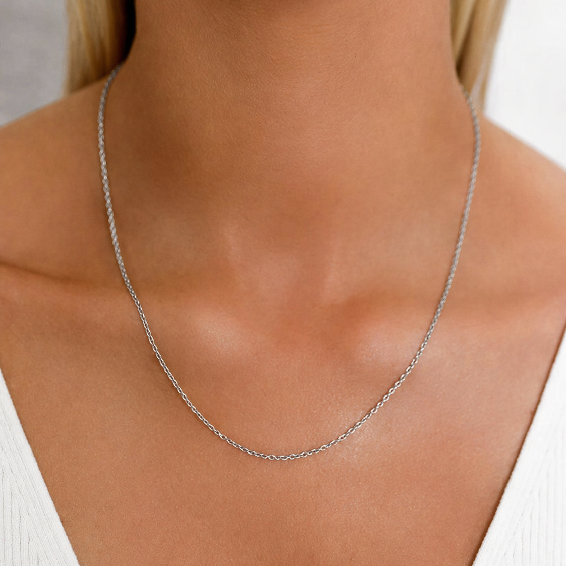 Silver necklace on a person wearing a white top against a neutral background