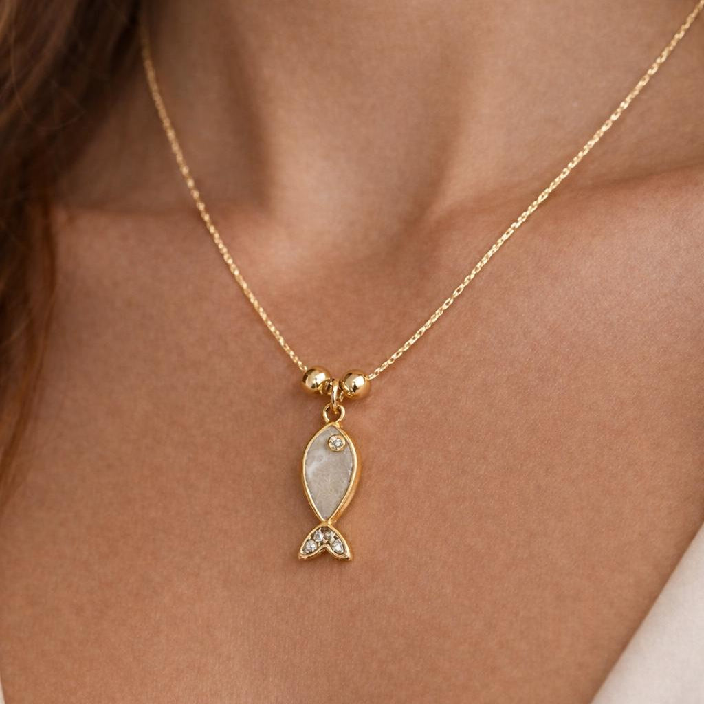Gold necklace with a fish-shaped pendant on a person's neck