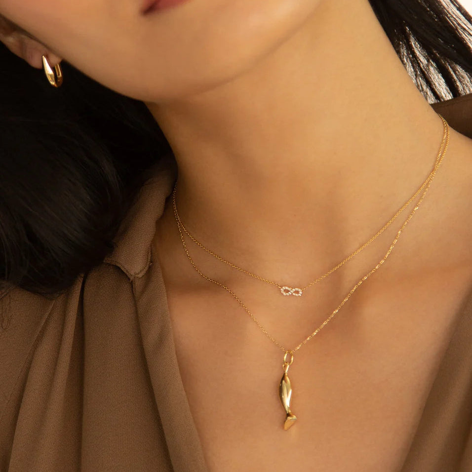 Close-up of a person wearing a gold necklace with a fish pendant.