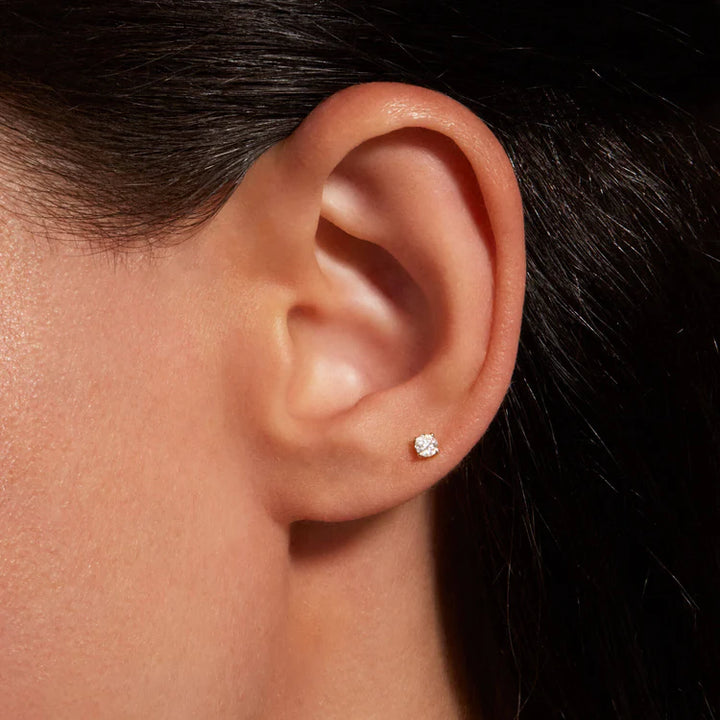 Close-up of an ear wearing a diamond stud earring with dark hair background
