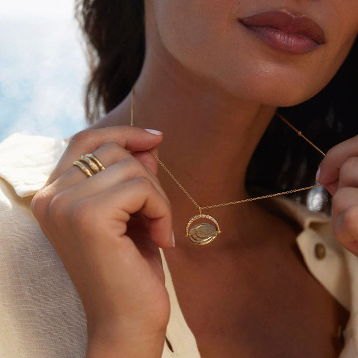 Close-up of a person wearing a gold necklace with a pendant, held by hands.